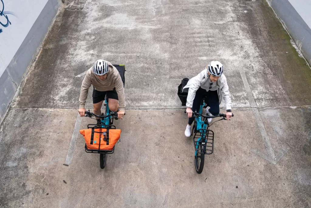 Discover the convenience and sustainability of Lug+Carrie's Tern Quick Hauls - see from above as a male and a female rider glide on concrete roads effortlessly, enjoying a stress-free commute.