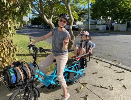 Lisa and her daughter sitting their Lug+Carrie eBike. They are outside on a warm autumn day. They have packed items onto their bike to go on a picnic at the park.